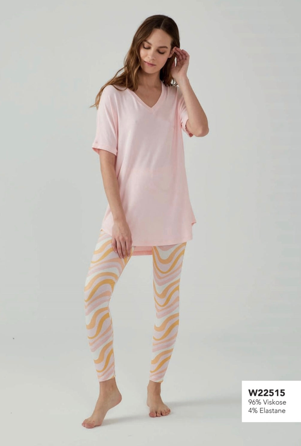 Model wearing Popjammies pink pyjama set with V-neck top and pastel pink and yellow wave-patterned leggings, standing against a plain background.