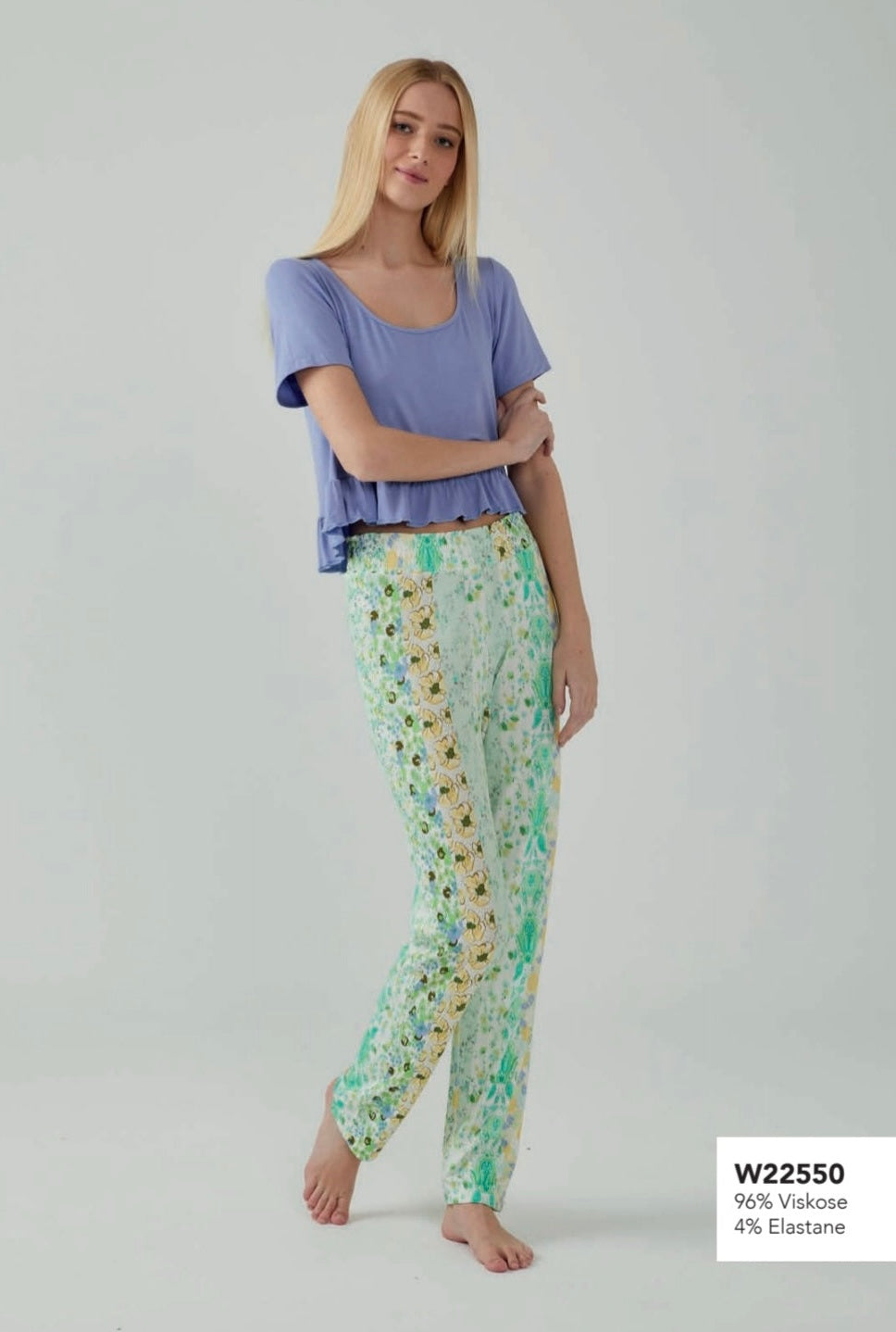 Model wearing a Popjammies floral trim pyjama set, featuring a lavender top with a ruffled hem and green floral print pants with yellow and blue flower trim.