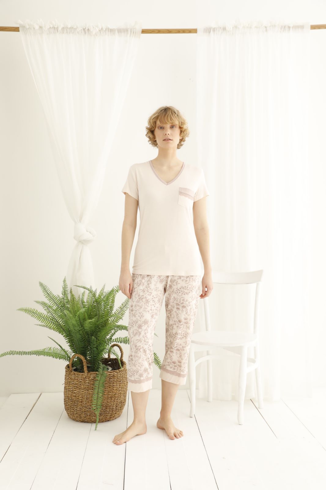 Woman wearing a beige short-sleeve V-neck top with pocket detail and floral patterned capri pants from the Popjammies Women's Short Sleeve V-Neck Top with Floral Capri Pyjama Set.