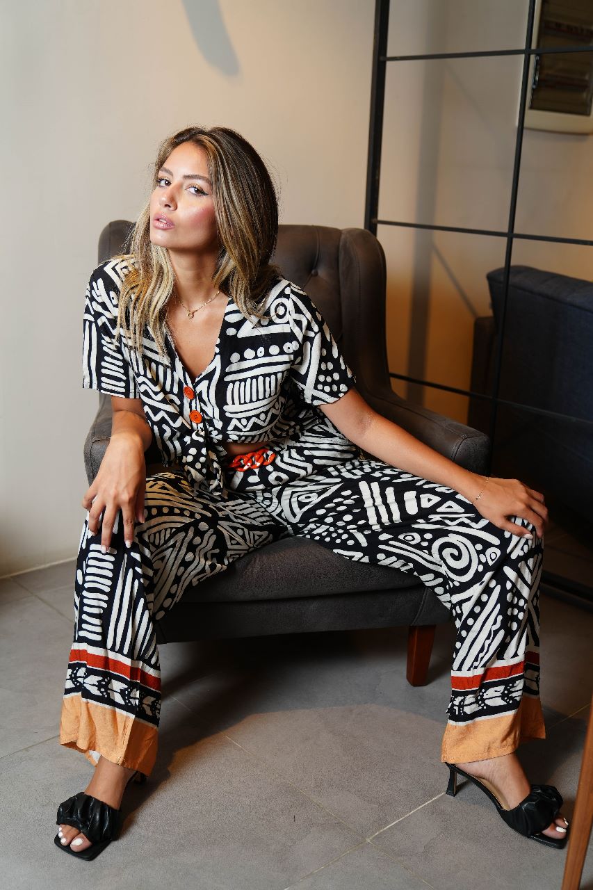 Model sitting on a grey chair wearing a Popjammies black and white tribal print pyjama set with orange button accents.