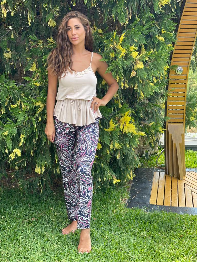 Model wearing a paisley print pyjama set by Popjammies, featuring a beige top and paisley print pants, standing outdoors with lush greenery in the background.