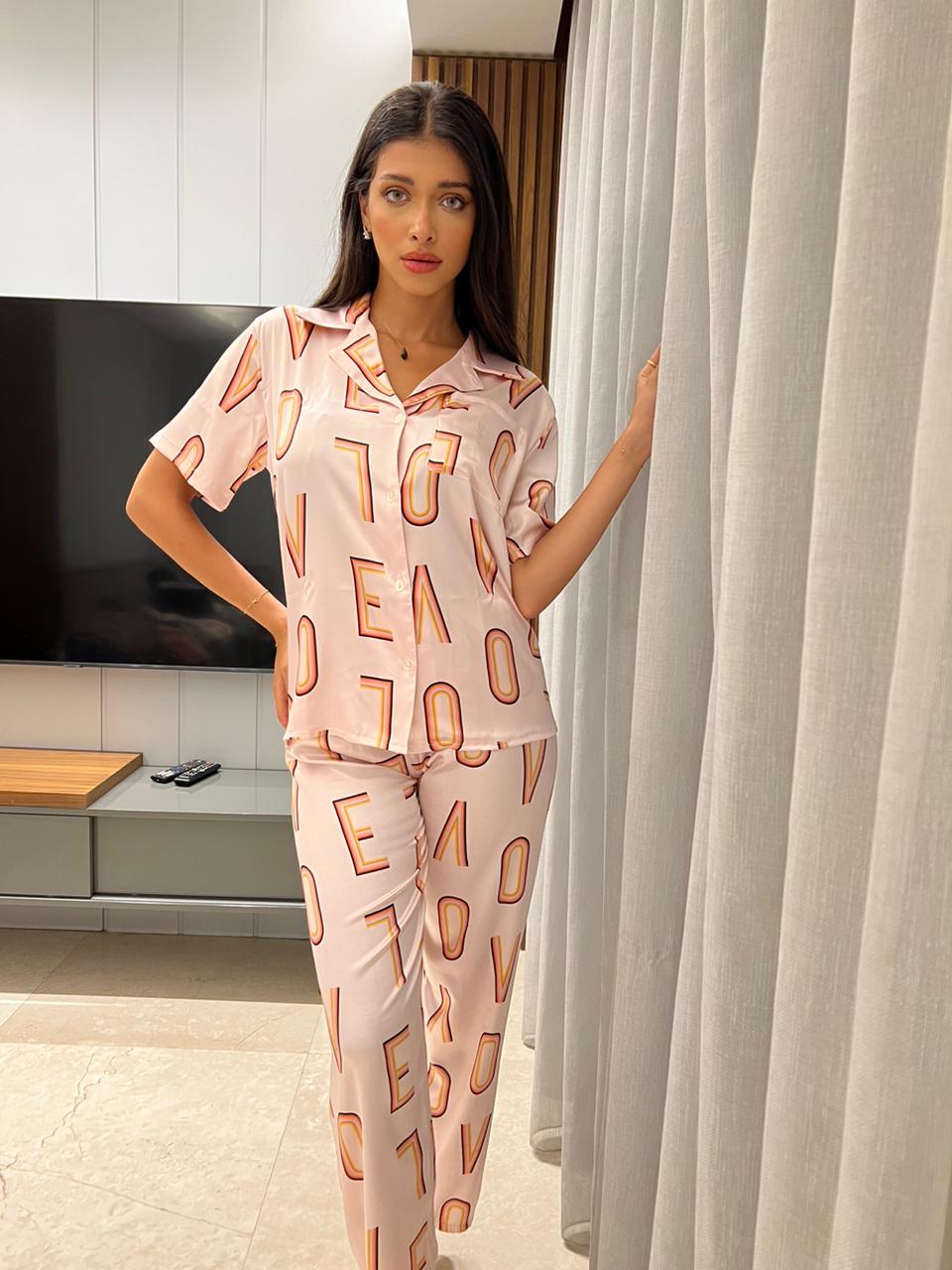 Model in a pink satin pyjama set with "LOVE" print by Popjammies, standing next to a curtain.