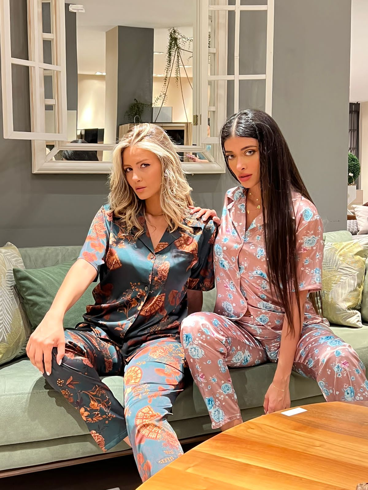 Two models sitting on a sofa, wearing floral print satin pyjama sets by Popjammies.