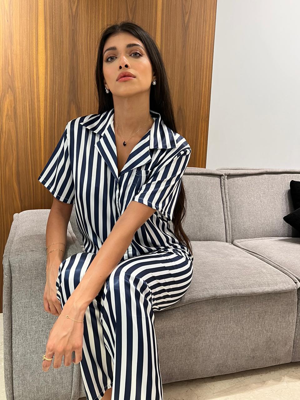 Model seated on a grey sofa, wearing a navy blue and white striped satin pyjama set by Popjammies.