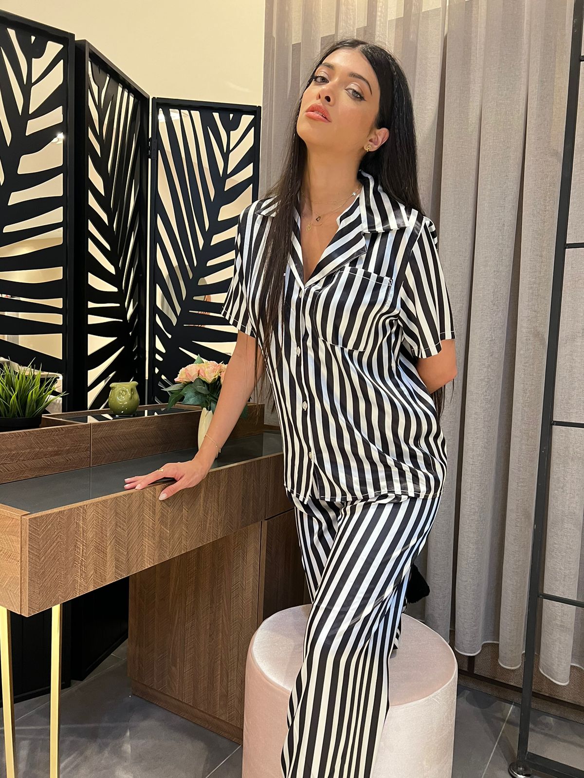 Woman in black and white striped satin pajamas, posing beside a modern vanity table.