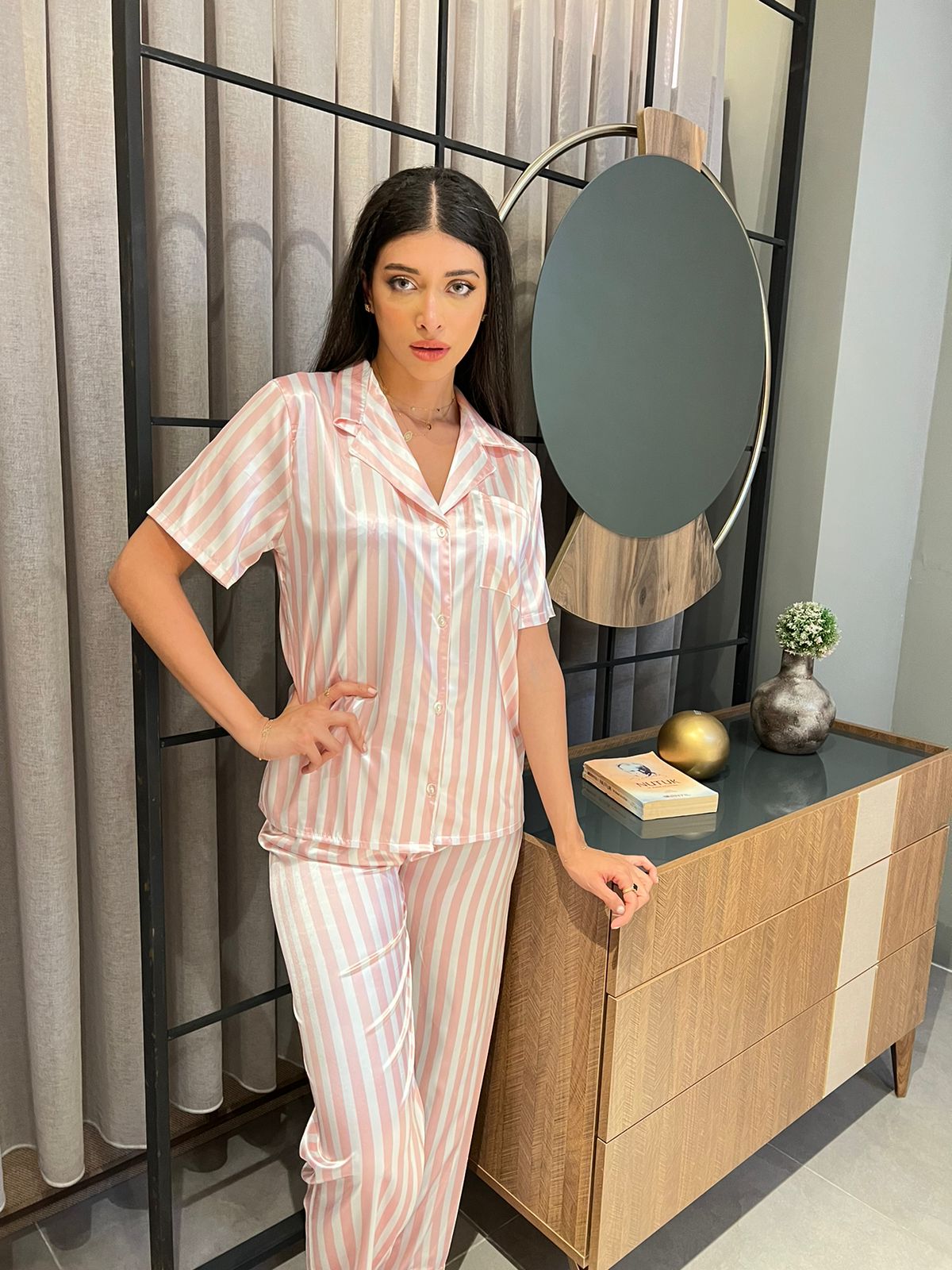 Model standing next to a mirror, wearing a pink and white striped satin pyjama set by Popjammies.