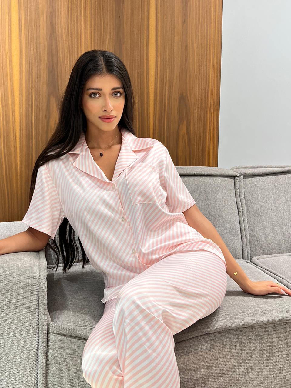 Model seated on a grey sofa, wearing a pink and white striped satin pyjama set by Popjammies.