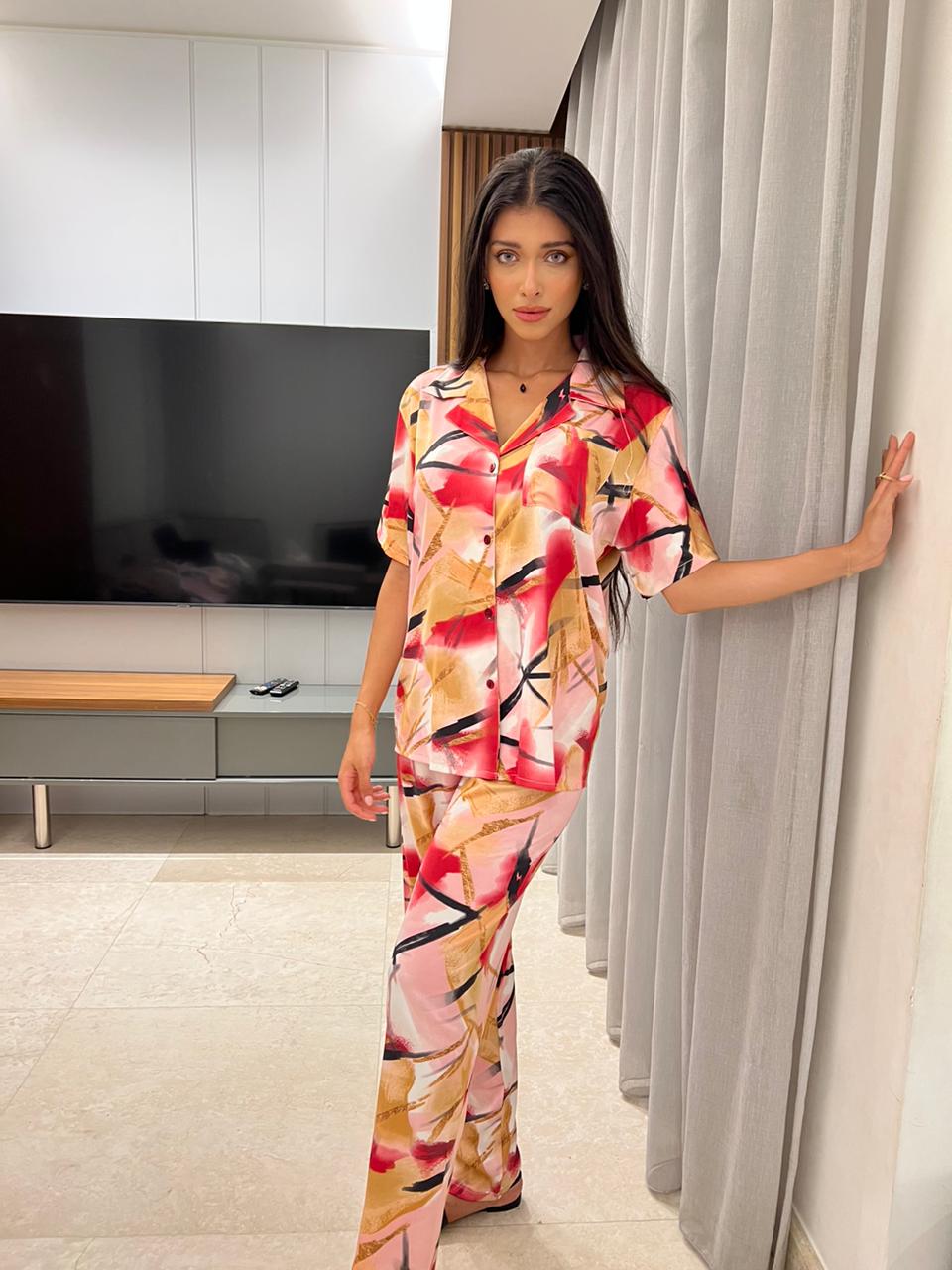 Model wearing a colorful abstract print satin pyjama set by Popjammies, standing against a TV.