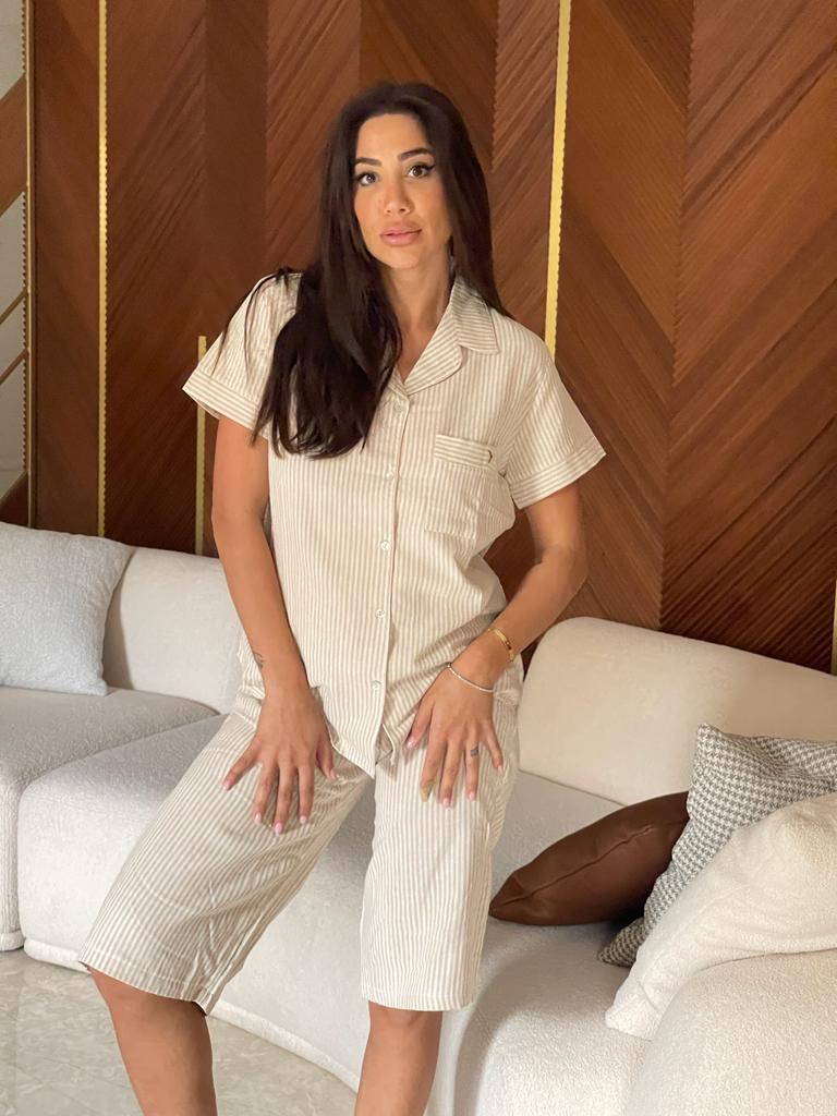 Woman posing in a beige short-sleeve button-down top with vertical stripes and matching capri pantacour.