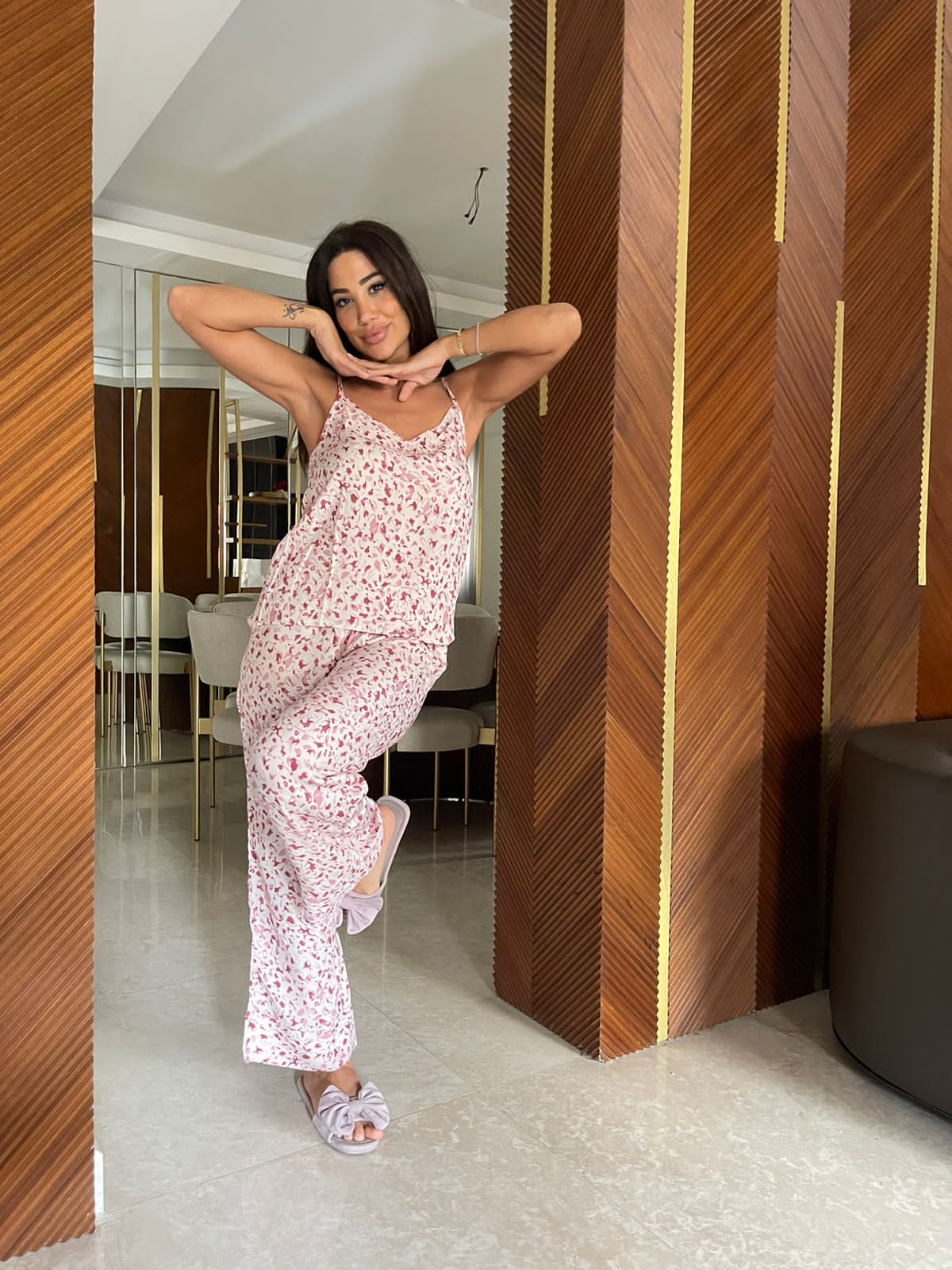 Woman striking a playful pose while wearing a pink floral camisole pajama set by Popjammies, in a stylish room with wooden accents.