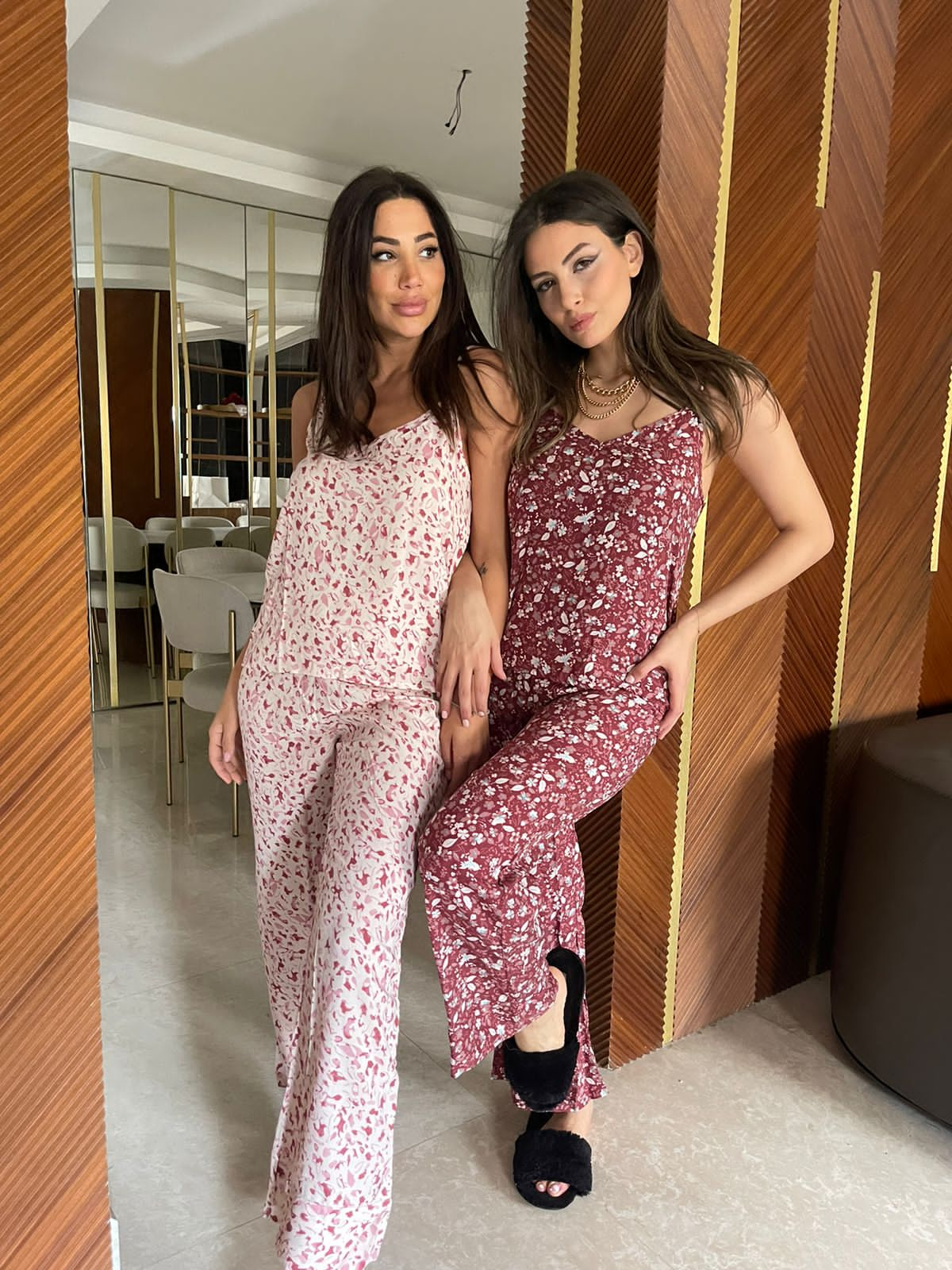 Two women posing in stylish floral print pyjamas. The woman on the left is wearing a white and pink floral pyjama set, while the woman on the right is wearing a maroon floral pyjama set.