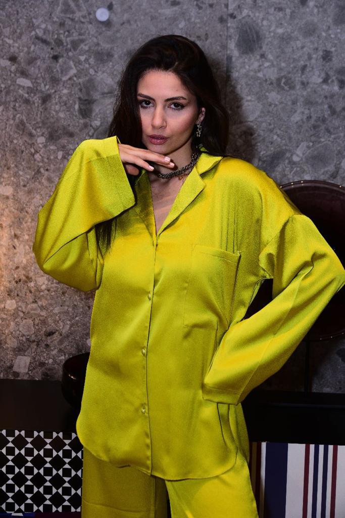 Model wearing a luxurious yellow silk pyjama set by Popjammies, striking a confident pose against a modern stone background.