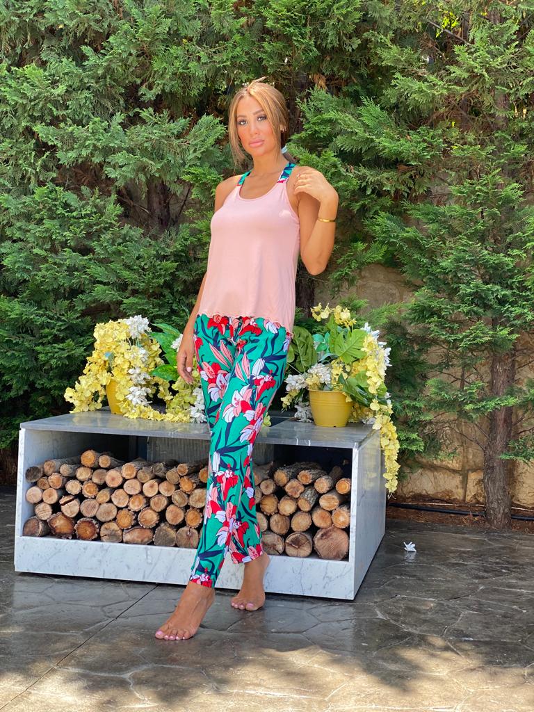 Woman wearing the Tropical Floral Pajama Set by Popjammies, featuring a sleeveless light pink top and bold, tropical floral-print pants with vivid green, red, and white flowers.