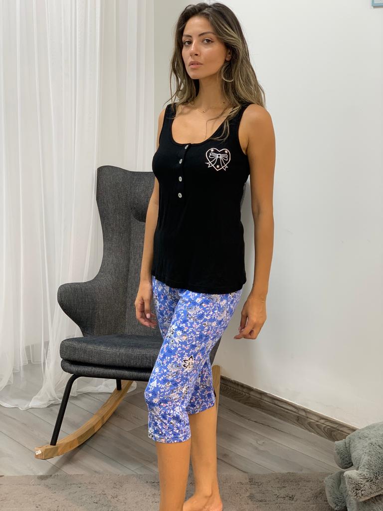 Woman wearing a black tank top paired with blue floral print capri pantacour by Popjammies, standing indoors near a grey chair.