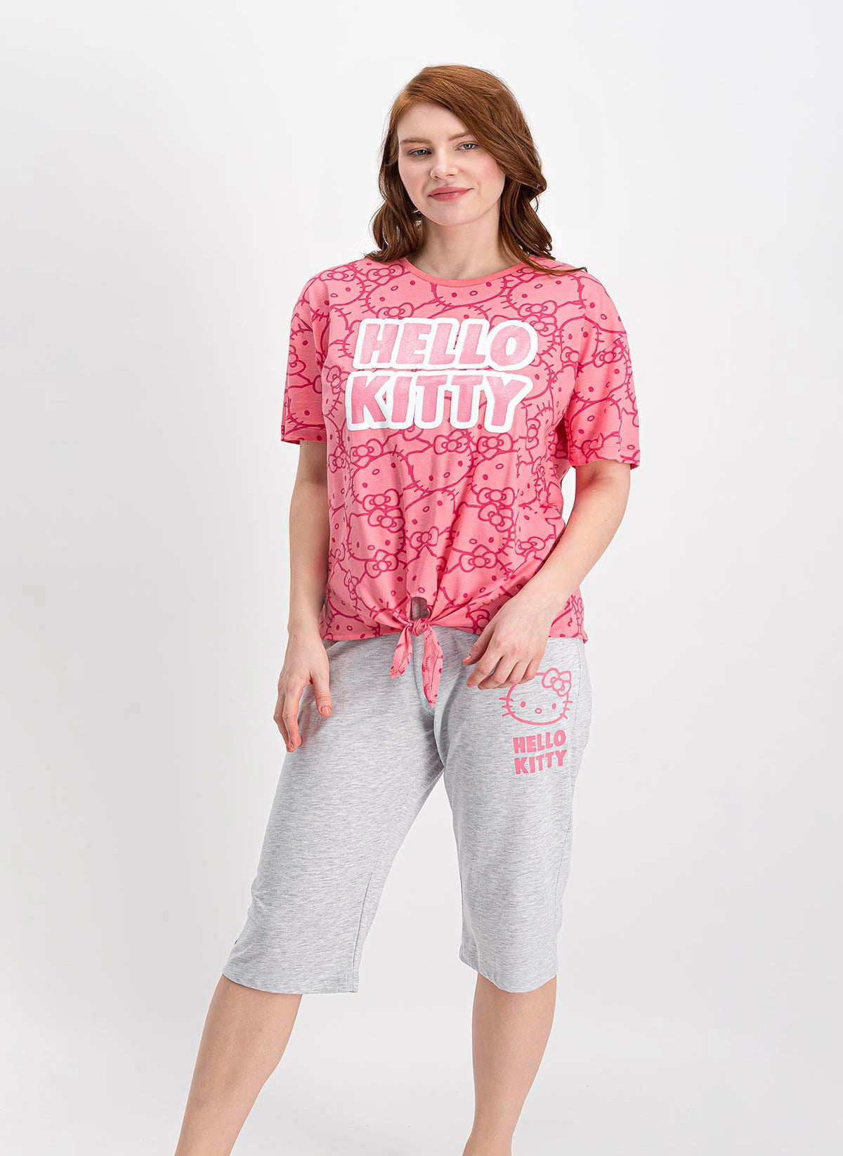 Woman wearing a pink short-sleeve top with Hello Kitty print and tie-front detail, paired with grey capri pantacour with a Hello Kitty graphic