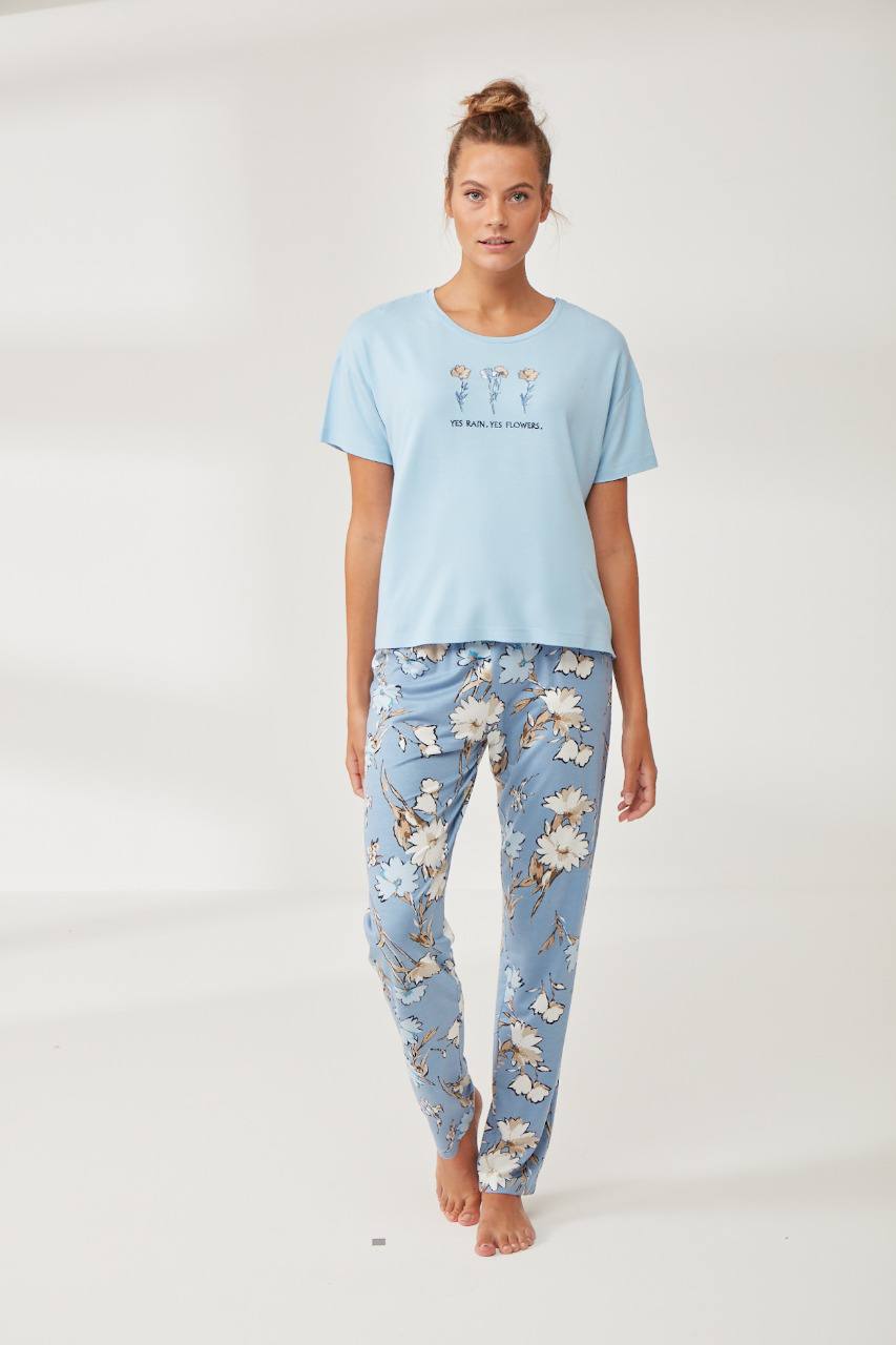 A woman wearing a blue t-shirt with "Yes Rain, Yes Flowers" text and matching floral pants, posing against a plain background.