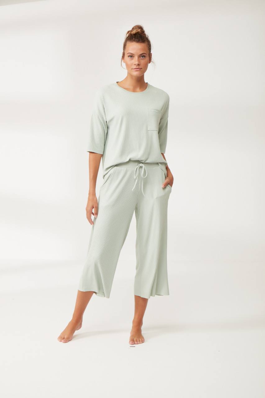 Woman wearing a sage green ribbed pyjama set with three-quarter sleeves, chest pocket, and wide-leg capri pantacour from Popjammies 