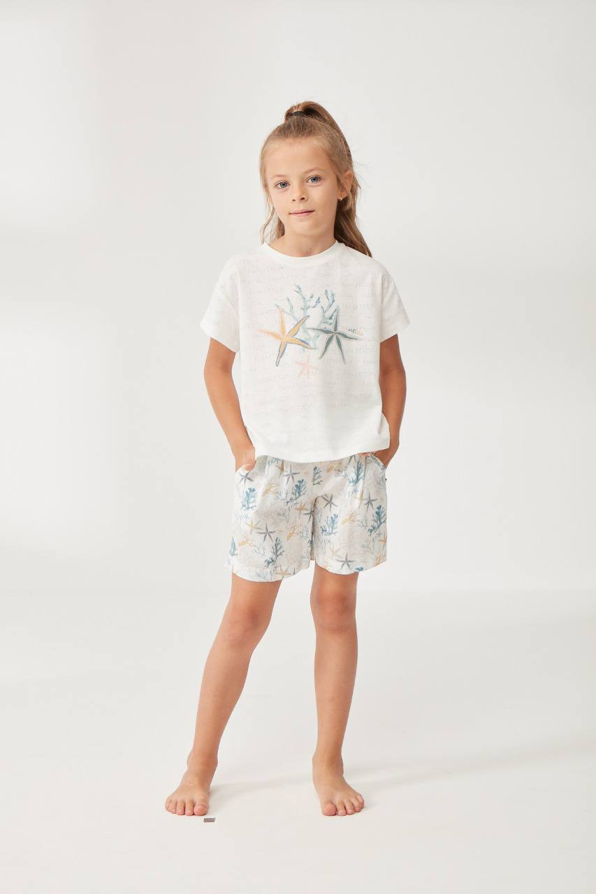 Girl wearing a white t-shirt with a starfish and coral reef design paired with matching sea-themed shorts from Popjammies.