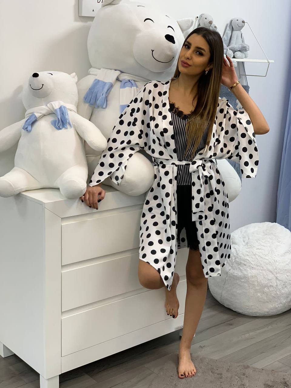 Model wearing a stylish striped and lace pyjama set with a polka dot robe by Popjammies, standing next to large white teddy bears in a cozy, modern room.